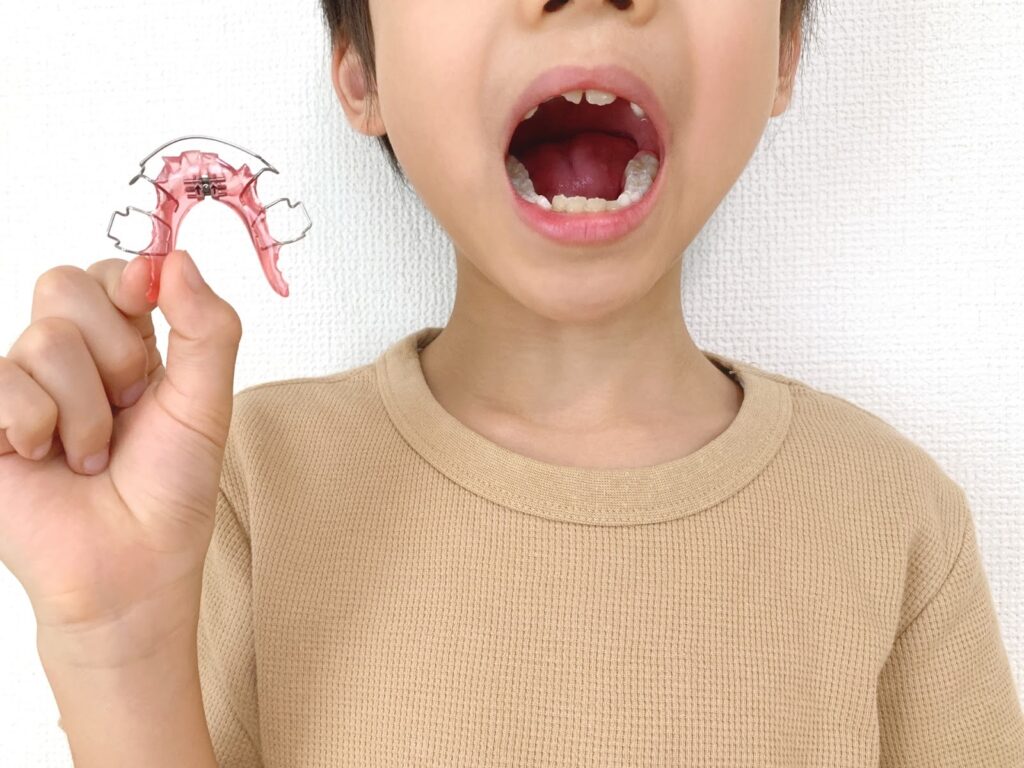 小児矯正で使用する矯正装置を手に持つ子どもの画像